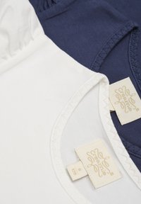 Twee katoenen T-shirts: één wit, één marineblauw. Beide hebben een ronde halslijn en gestikte zomen. Labels zijn zichtbaar met de "Creamie" branding.