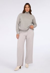 Maglione dolcevita grigio chiaro abbinato a pantaloni a gamba larga grigio pallido. I pantaloni presentano spacchi laterali e un motivo a trama sottile. Scarpe crema con tacco a blocco.