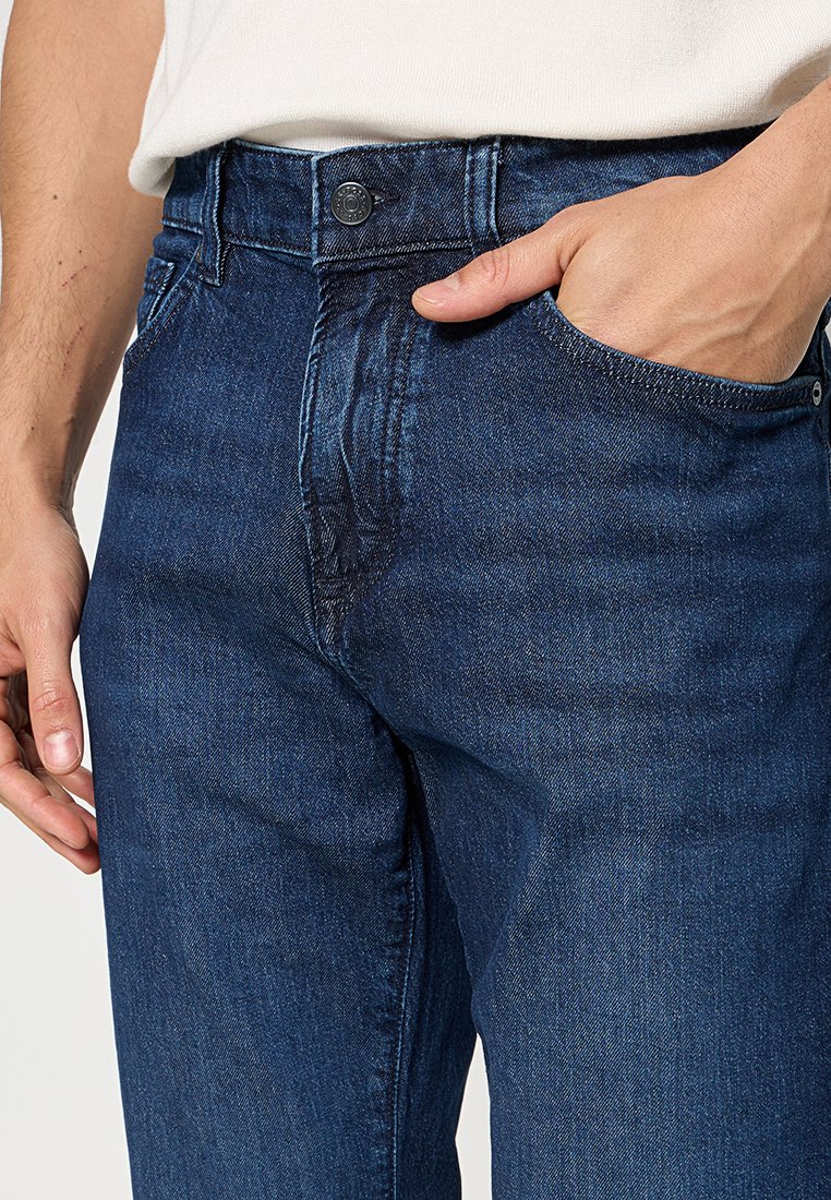 Jean en denim bleu avec une coupe droite, fermeture à bouton et poches avant. Le tissu présente une texture subtile avec un léger délavage.