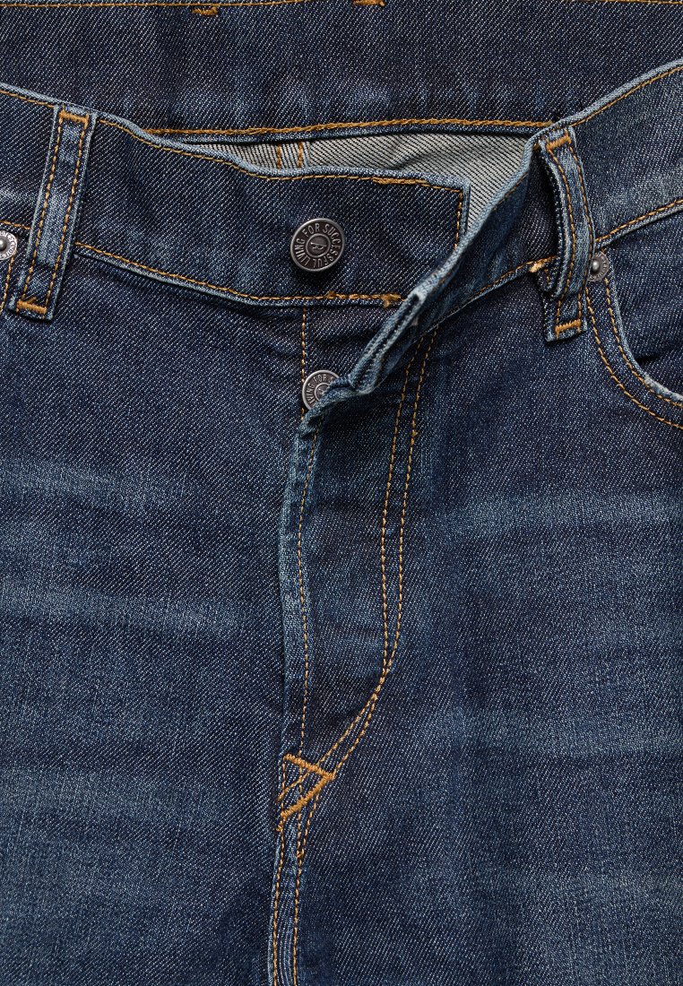 Dunkelblaue Jeans aus Denim mit teilweise geöffnetem Knopfverschluss, der silberne Knöpfe und orangefarbene Kontrastnähte zeigt.