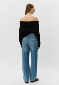 Melnas plecu džemperis, kas apvienots ar gaiši zilām platām kājām beigās izbalējušām biksēm ar divām aizmugurējām kabatām. Gluda tekstūra, minimāla apdare.