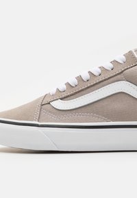 Baskets en toile beige avec des lacets blancs, dotées d'une bande latérale blanche, d'une bordure noire et d'une semelle en caoutchouc texturée. Design minimaliste.