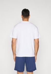 Hvid bomulds t-shirt med korte ærmer og rund hals, vist fra bagsiden, parret med mørkeblå shorts. Enkel, glat tekstur.