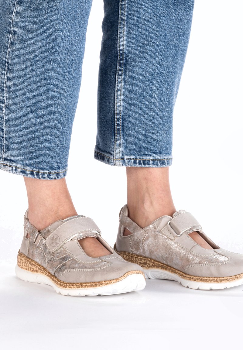 Helle graue Schuhe mit einer flexiblen Sohle, T-Riemen-Design, Klettverschluss und seitlichen Ausschnitten. Korkstrukturierte Akzente an der Basis.