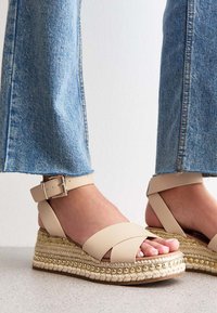 Beiga espadrilleplattform sandaler med korsade remmar, vävd jute-sula och metallpärla, kombinerat med vida denimjeans.