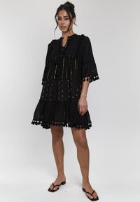 Abito nero a strati con maniche corte, realizzato in tessuto traforato e decorazioni con frange. Presenta strisce metalliche e pois su tutta la superficie.