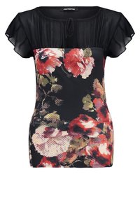 Bloemen-t-shirt met een zwarte chiffon overlay en korte fluttermouwen. Levendig rood en groen bloemenpatroon op een donkere achtergrond.