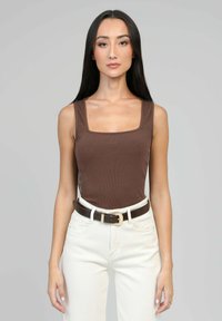 Débardeur marron à côtes avec décolleté carré, associé à un pantalon blanc taille haute et une ceinture marron foncé avec une boucle dorée.