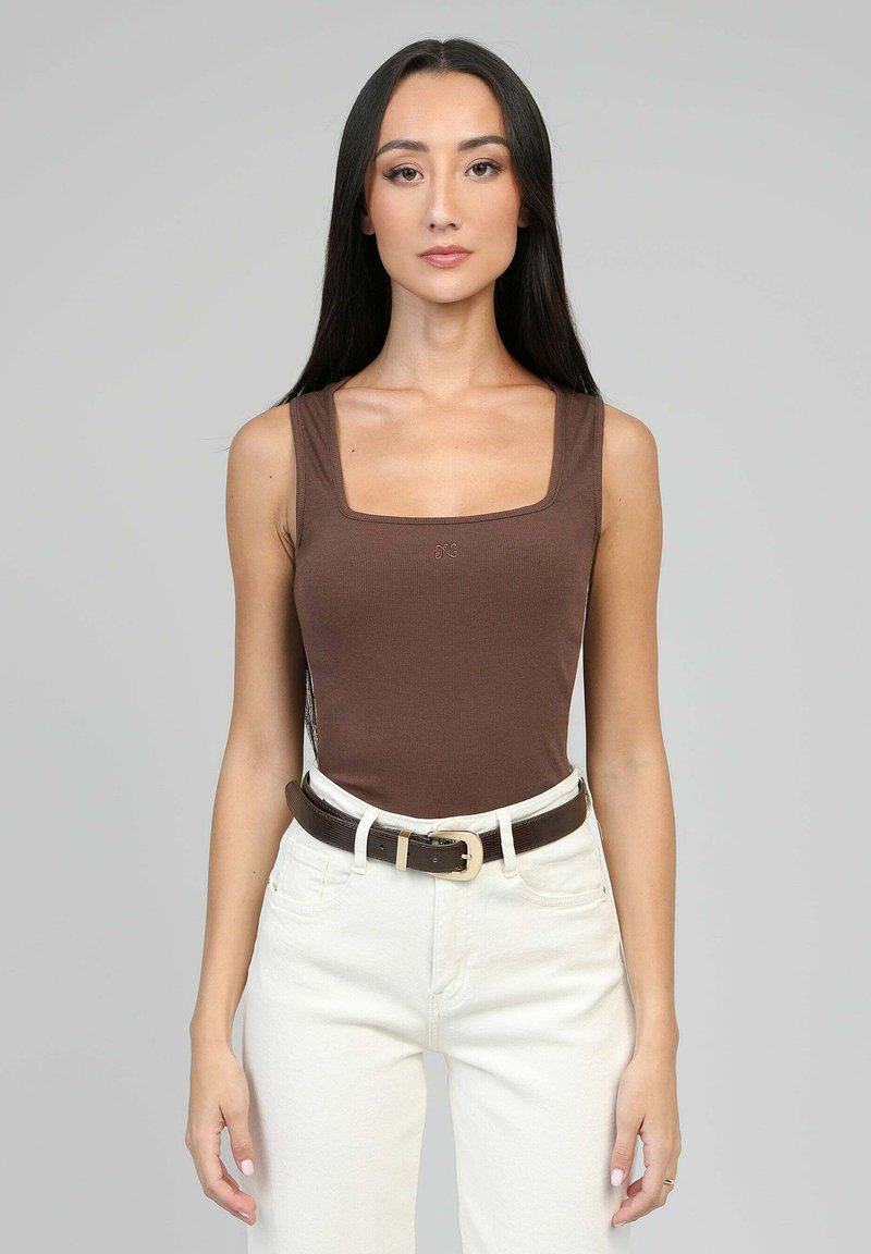 Débardeur marron à côtes avec décolleté carré, associé à un pantalon blanc taille haute et une ceinture marron foncé avec une boucle dorée.