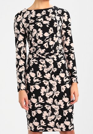 Schwarzes knielanges Kleid mit langen Ärmeln, blassrosa Blumenmuster und dezenten Raffungen an der Taille, getragen von einer Person vor schlichtem Hintergrund.