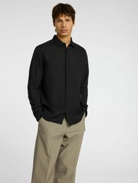 Camisa negra de manga larga con botones, hecha de una tela ligera, combinada con pantalones de pierna ancha beige. Presenta un cuello clásico y botones frontales.