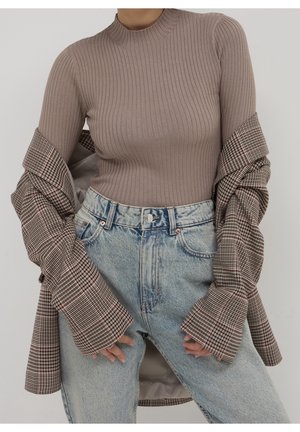 Personne portant un col roulé côtelé taupe, un jean taille haute bleu clair et une veste à carreaux marron avec les manches baissées.