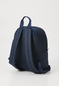 Zaino navy realizzato in tessuto con spallacci imbottiti, una piccola maniglia superiore e una superficie liscia. Caratterizzato da un design semplice e lineare.