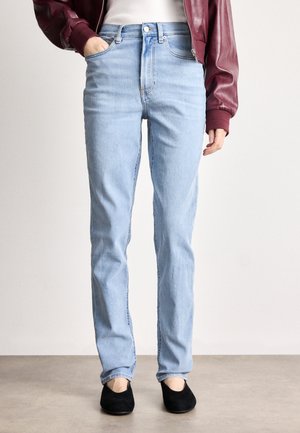 Lyseblå højtaljede jeans med lige ben, lavet af denim. Sammen med sorte slip-on sko og en bordeaux læder bomberjakke.