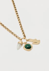 Κολιέ με χρυσή αλυσίδα και τρία μενταγιόν: λευκό σε σχήμα δοντιού, πράσινη πέτρα σε χρυσό πλαίσιο, και χρυσή φιγούρα κροκοδείλου σε λευκό φόντο.