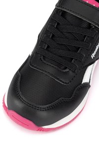 Juodas Reebok sportbaikis su juodais raišteliais, balta šonine juostele ir rožiniu padu priekyje, demonstruojantis išsamią siuvimo ir tekstūros detalę.