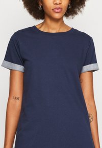 T-shirt bleu marine en tissu doux, avec des manches courtes et des poignets contrastants de style denim, ainsi qu'un col rond classique.