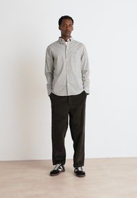 Camicia button-up a quadri in verde chiaro e bianco, abbinata a pantaloni in velluto a coste verde scuro e sneakers nere. Design semplice e vestibilità rilassata.