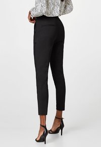 Svarta skräddarsydda byxor med smal passform, som har en medelhög midja, sidofickor och detaljer på bakfickan, kombinerade med svarta strap-heeled skor.