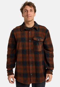 Karierte Flanellhemd in Braun, Marineblau und Grün. Verfügt über einen Button-Down-Kragen, eine einzelne Brusttasche und schwarze Druckknöpfe. Weicher Stoff.