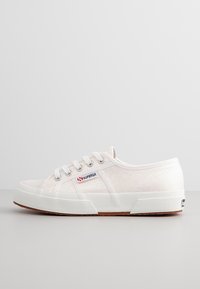 Baskets en toile blanches avec un dessus texturé, six oeillets, lacets blancs et une semelle en caoutchouc avec une semelle en gomme. Logo Superga sur le côté.
