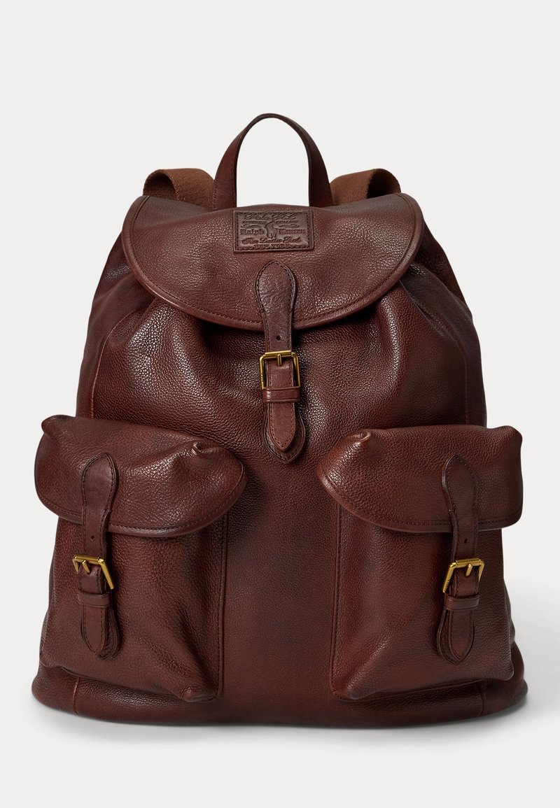 Brown leather backpack with flap closure, two front pockets with buckle straps, and a top handle.