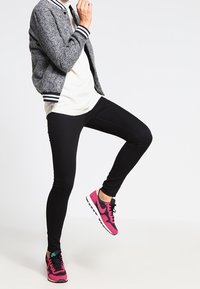 Sorte skinny jeans kombinert med en hvid top og en grå bomberjakke. Skoene er rosa og sorte Nike sneakers med blå detaljer.