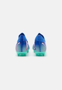 Blue soccer cleats with a textured, gradient design, featuring a turquoise sole and pink accents on the sides. Designed for performance.