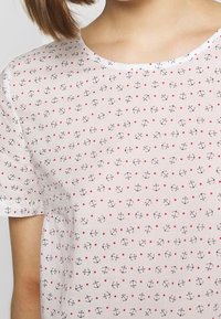 Biała bluzka z krótkim rękawem w ciemne kotwice i wzór czerwonych kropek, z okrągłym dekoltem i lekkim, strukturalnym materiałem.