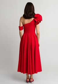 Czerwona sukienka midi z asymetrycznym dekoltem, dużym detalem falbany oraz dopasowaną górą. Zamek błyskawiczny z tyłu i rozkloszowany dół.
