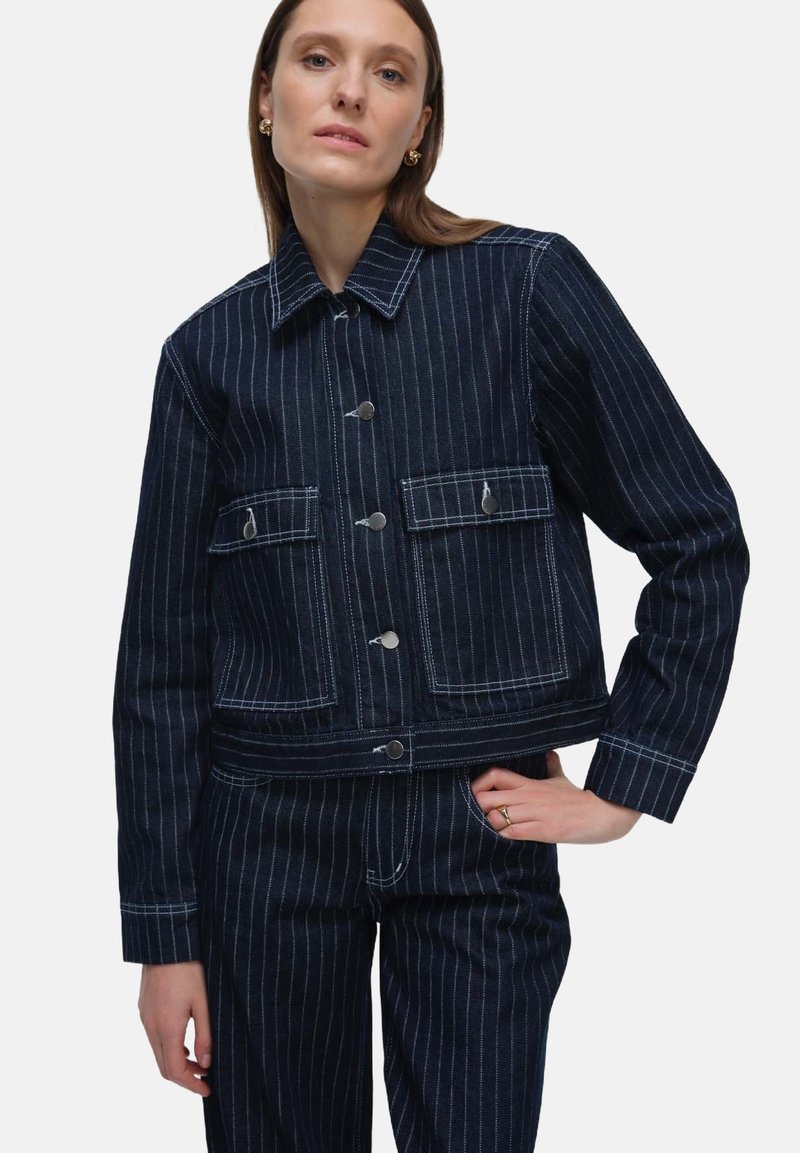 Niebieska jeansowa kurtka z białymi paskami, skrócona konstrukcja, przednie kieszenie i przyciski w srebrnym odcieniu. Teksturowany materiał, luźny krój.