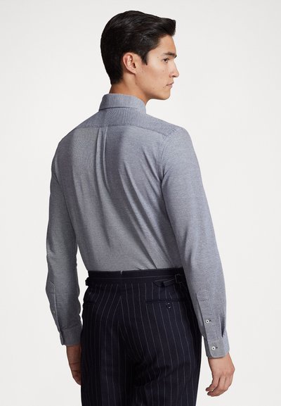 Grijze langarmshirt met verhoogde kraag, voorzien van een gestructureerde stof en knoopsluiting bij de manchetten, gecombineerd met donker gestreepte broek.