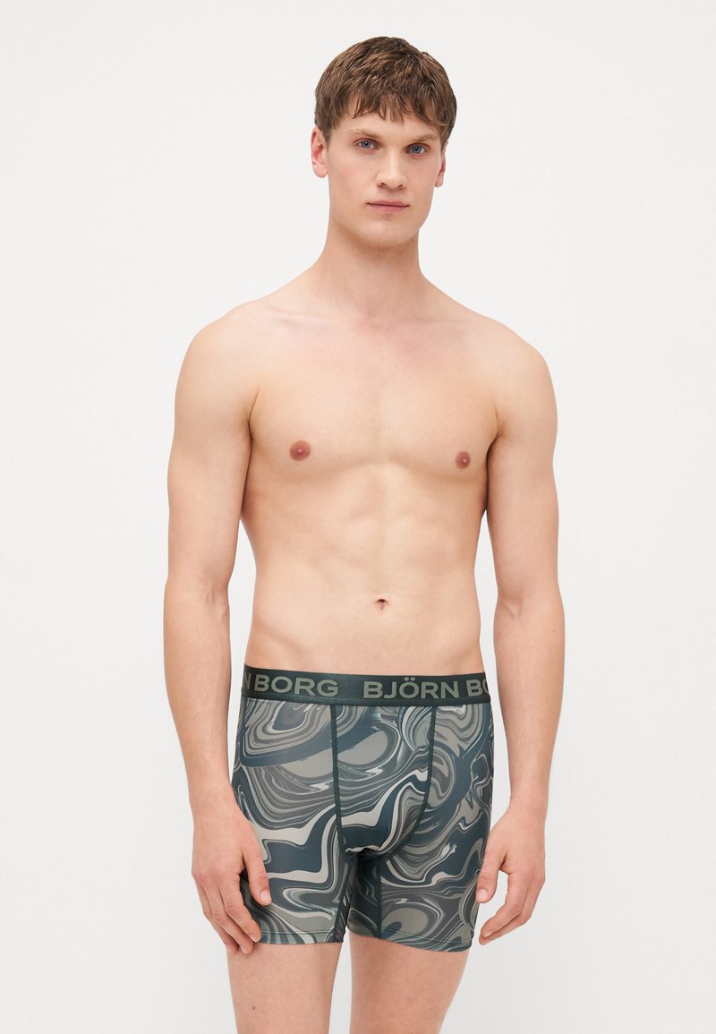 Boxers justos em verde e cinza mármore com uma cintura elástica de marca, feitos de um tecido elástico. O design apresenta uma textura suave e uma forma ajustada.