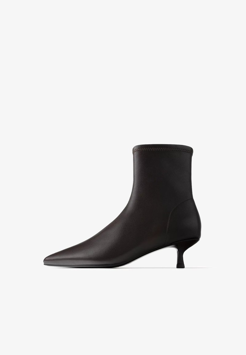 Bottine en cuir noir à bout pointu et petit talon kitten, design minimaliste élégant sur fond blanc.