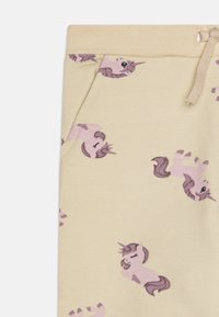 Pantaloni giallo chiaro con una texture morbida, decorati con illustrazioni di unicorni ripetute in rosa e viola, dotati di vita regolabile con cordoncino e tasca laterale.