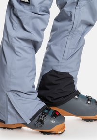 Grå skibukser med en tætsiddende pasform, sorte accentpaneler og sidelommer. Mørkegrå ski-støvler med justerbare spænder og orange såler.