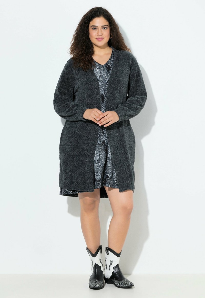 Cardigan in carboncino in maglia morbida con maniche lunghe e apertura frontale, abbinato a un vestito fantasia e stivali cowboy bianco e nero.