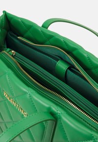 Grön vadderad läderhandväska med en gyllene dragkedja och detaljer, flera innerfack och stadiga handtag för bärning.