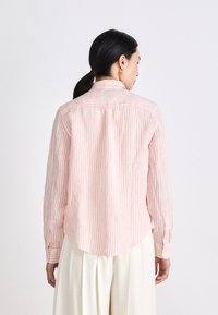 Striped shirt in pale pink and white, featuring a collar, long sleeves, and a curved hem. Made of lightweight fabric with visible stitching.