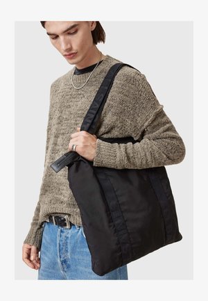 Svart nylon tote bag med teksturerte stropper som viser preget merkevare. Vesken har glidelås og myk, matt finish.