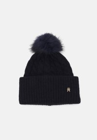 Beanie lavorato a maglia in blu navy con un bordo a coste e un motivo a treccia; presenta un grande pompon in pelliccia artificiale e una piccola accentuazione con logo dorato.