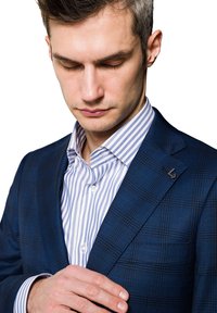 Niebieska marynarka w kratkę z klapami, noszona z białą koszulą w niebieskie paski. Ma czarną poszewkę na klapę oraz gładką fakturę.