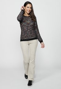 Pull en tricot multicolore avec un col rond et des manches longues. Associé à un jean évasé beige clair et des baskets noires.