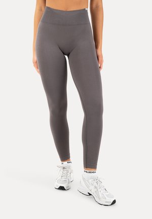 Nedre del af en person iført grå leggings med høj talje, hvide Smilodox-strømper og hvide atletiske sneakers, stående på en ensfarvet hvid baggrund.
