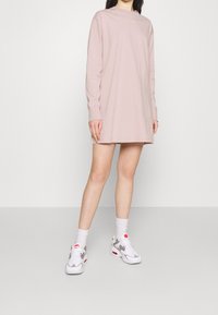 Rosa långärmad t-shirtklänning med rundad halsringning och Nike-logotyp, kombinerad med vita och grå sneakers samt ankelsockar.