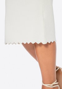 Witte geribbelde gebreide jurk met een gegolfde onderrand, met een aansluitende pasvorm en middelange lengte. Beige sleehak schoenen complementeren de outfit.