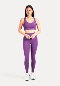 Lila sportbehå och högmidjade leggings av stretchigt material, med en slät textur och minimal logodetalj.