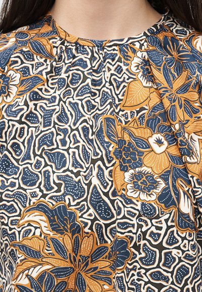 Κοντινό πλάνο σε ύφασμα με γαλάζια και μουσταρδί floral μοτίβα σε άσπρο φόντο με αφηρημένα σχήματα.