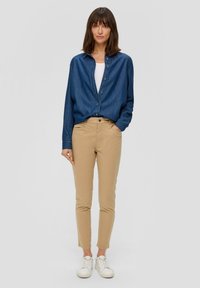 Kurtka denimowa zapinana na guziki w ciemnym niebieskim kolorze, kremowy top na ramiączkach, beżowe dopasowane spodnie i białe trampki. Prosty design o luźnym kroju.