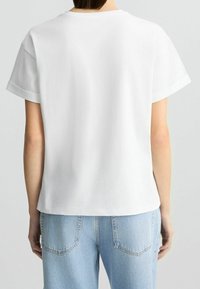 Weißes T-Shirt mit kurzen Ärmeln, entspanntem Schnitt, rundem Halsauschnitt und aufgerollten Bündchen, kombiniert mit hellblauen Jeans. Glatte Stofftextur.